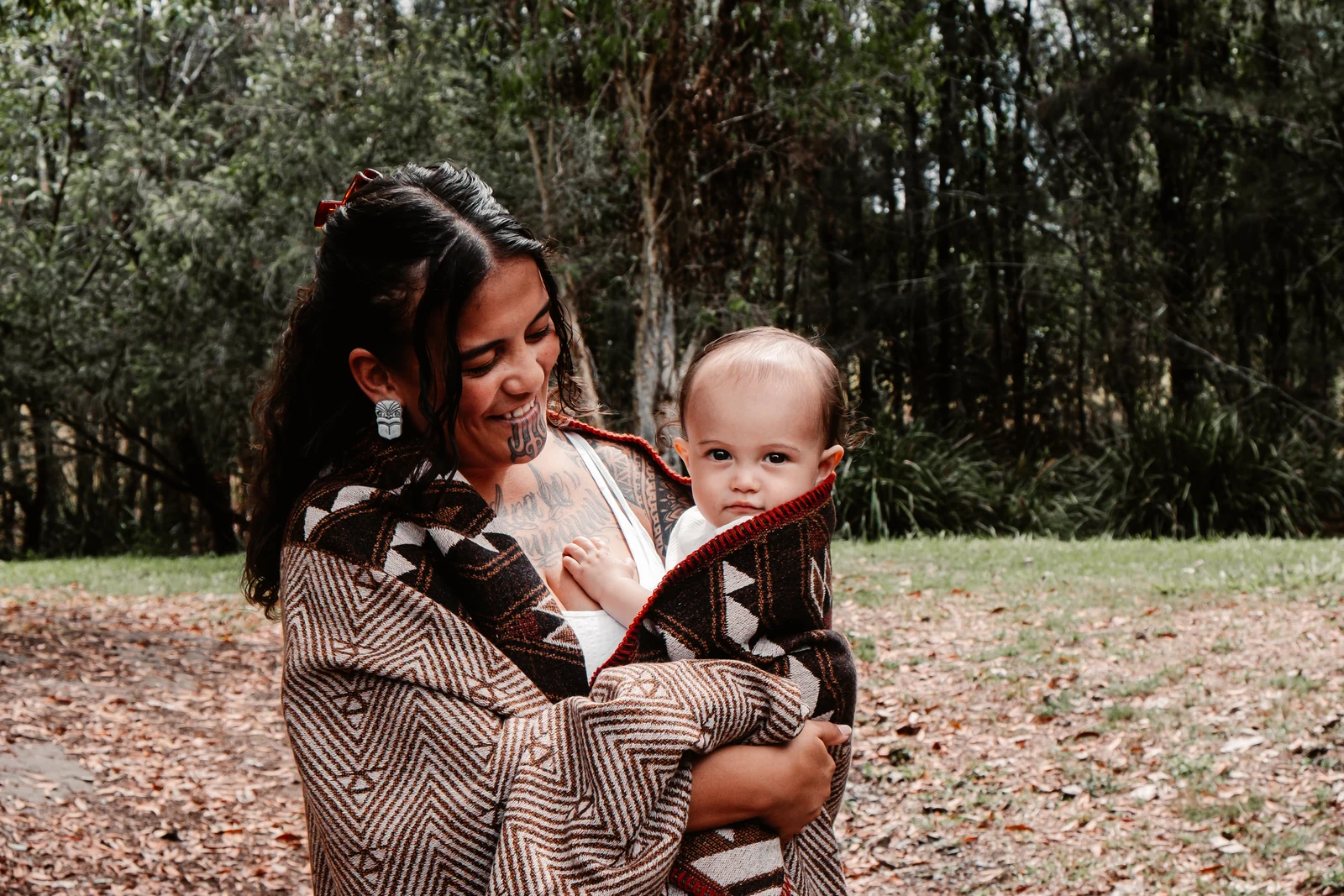Mum holding her baby wrapped together in a patterned blanket outdoors